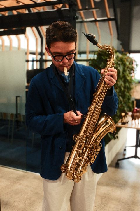 Saxophonist in a navy blazer and glasses playing among the office desks