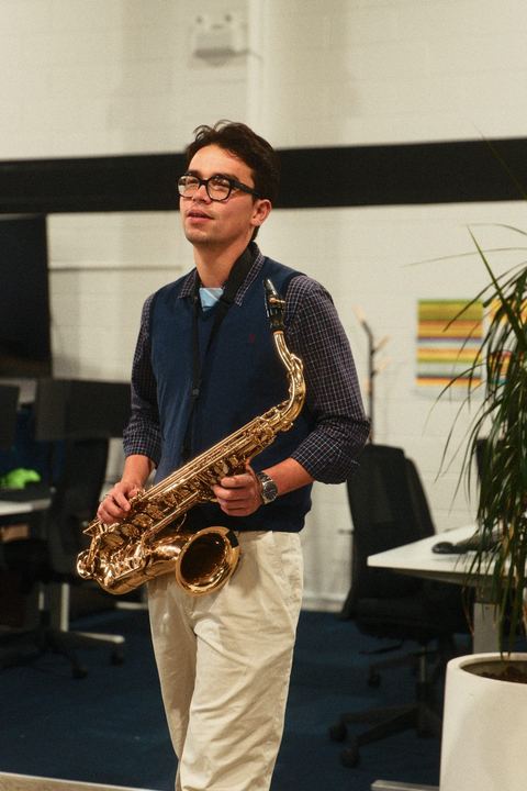 Saxophonist standing between rows of office desks