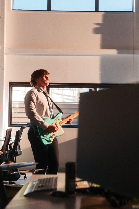 Guitarist playing a teal guitar beside the office monitors